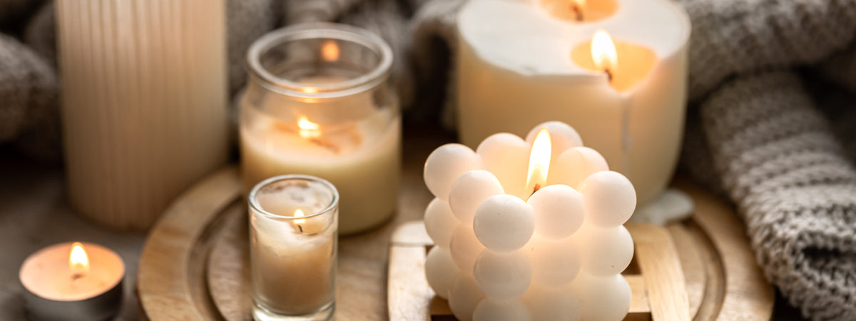 Lit white bubble candle styled with warm neutral candles on a wooden tray beside a cozy knit blanket for fall home decor.