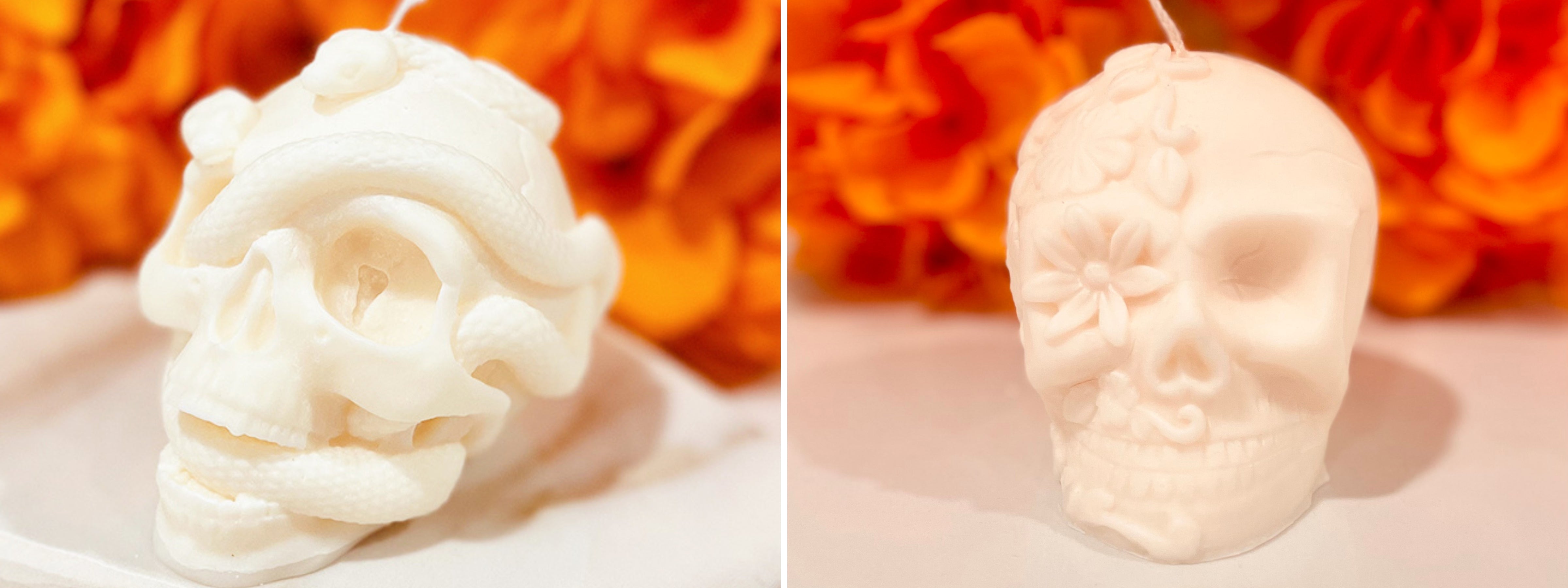 Two ivory sculpted skull candles—one wrapped in a coiled snake and the other adorned with floral patterns—styled against a backdrop of vibrant orange marigold flowers.