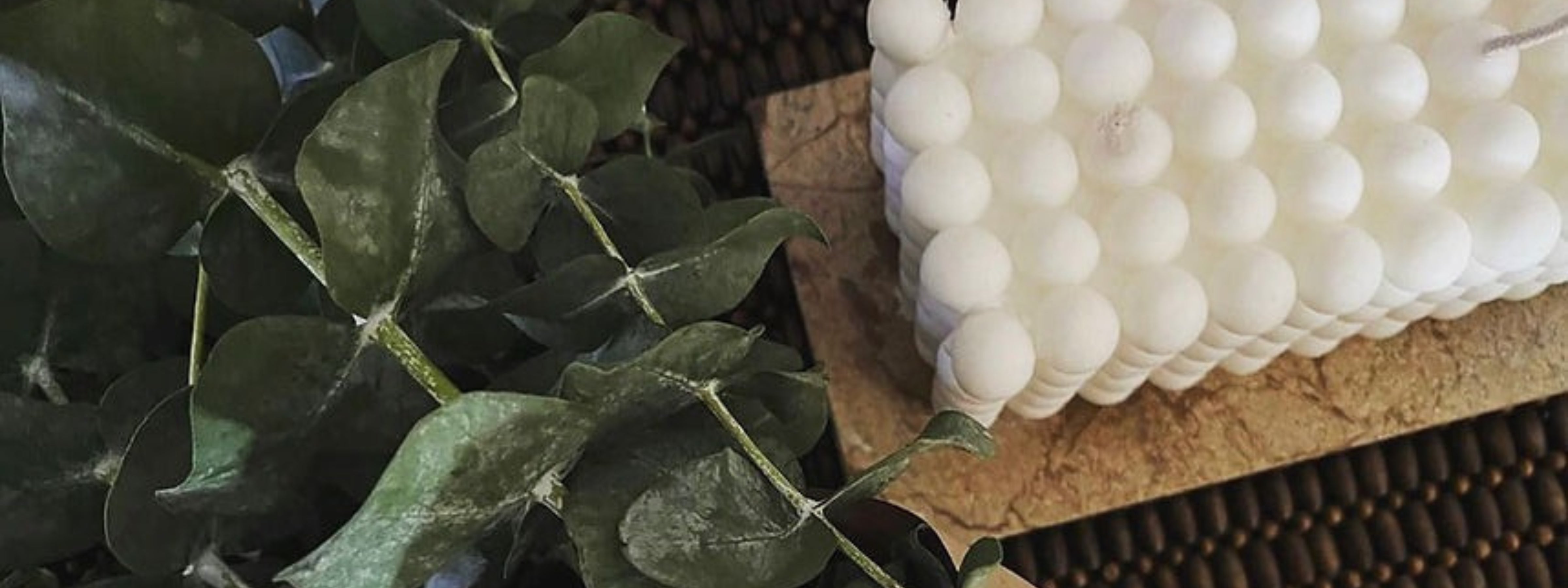 A white bubble-shaped candle sits on a textured stone tray beside a branch of green eucalyptus leaves, creating a cozy and minimalist fall-inspired decor setting.