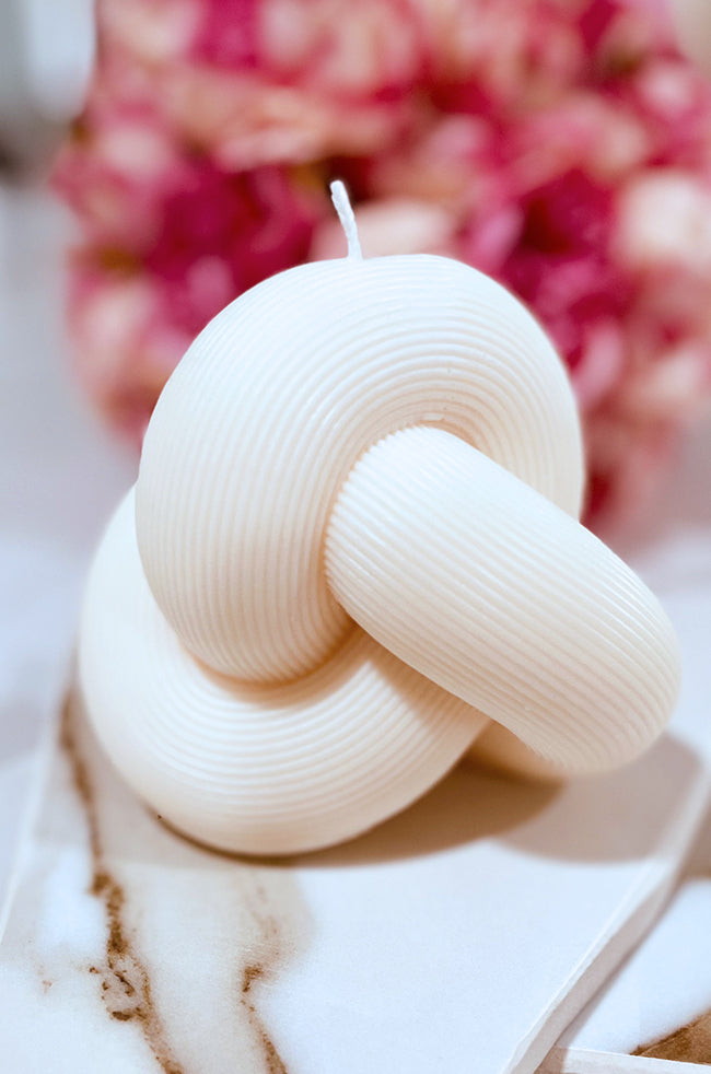 Serenity Knot Candle: Close-up of the ivory Serenity Knot sculptural candle with flowing ribbed loops displayed on marble.