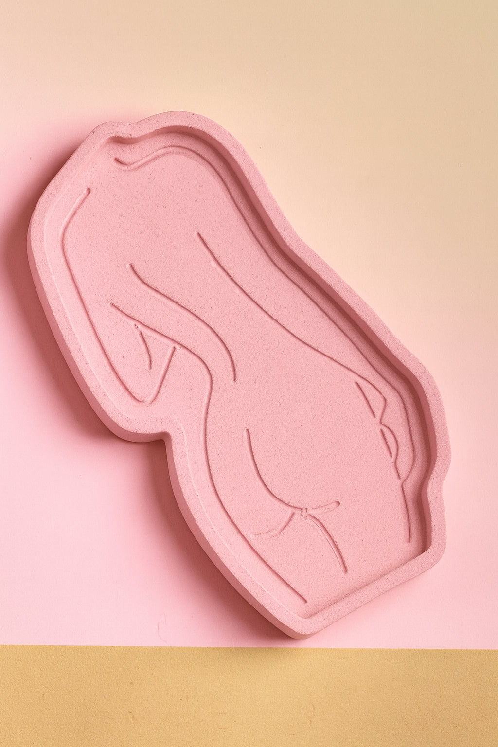 Daring Body Candle Tray: Pink sculpted candle tray in the shape of a female silhouette with minimalist line art detailing, placed on a pink surface.