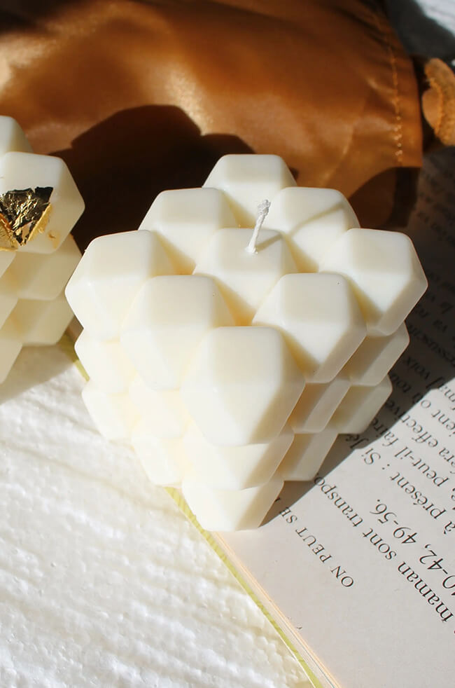 Diamonds Candle: White sculpted diamond-shaped candle placed on an open book with a silk pouch in the background.