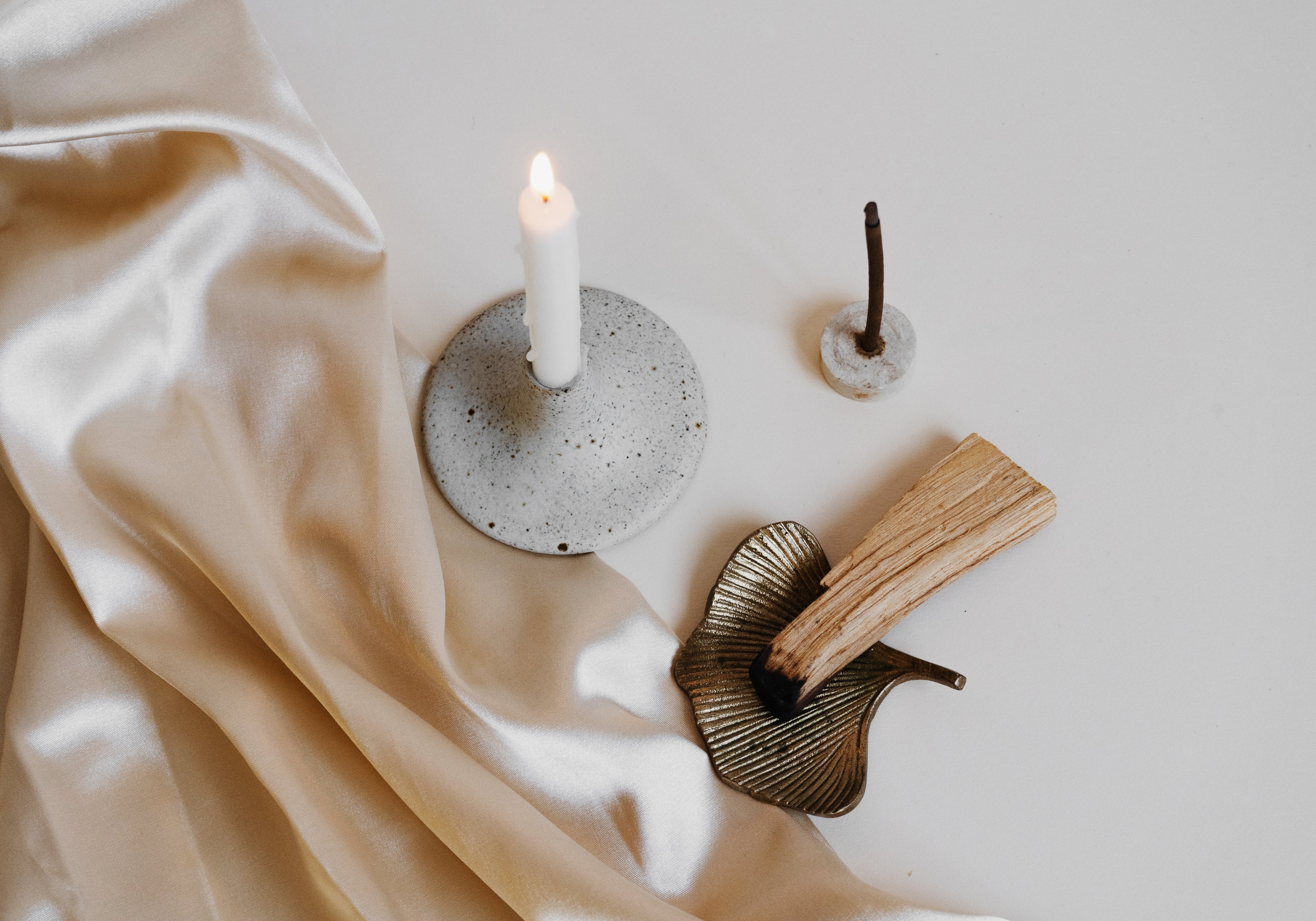 Lit taper candle beside palo santo and an incense holder on soft neutral fabric, creating a warm, minimalist fall scene.