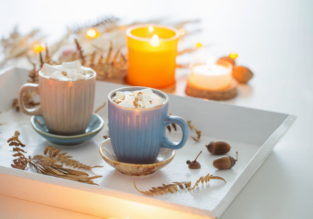 Two mugs of hot cocoa with marshmallows styled on a white tray with autumn leaves, acorns, and glowing candles for a cozy fall coffee table.
