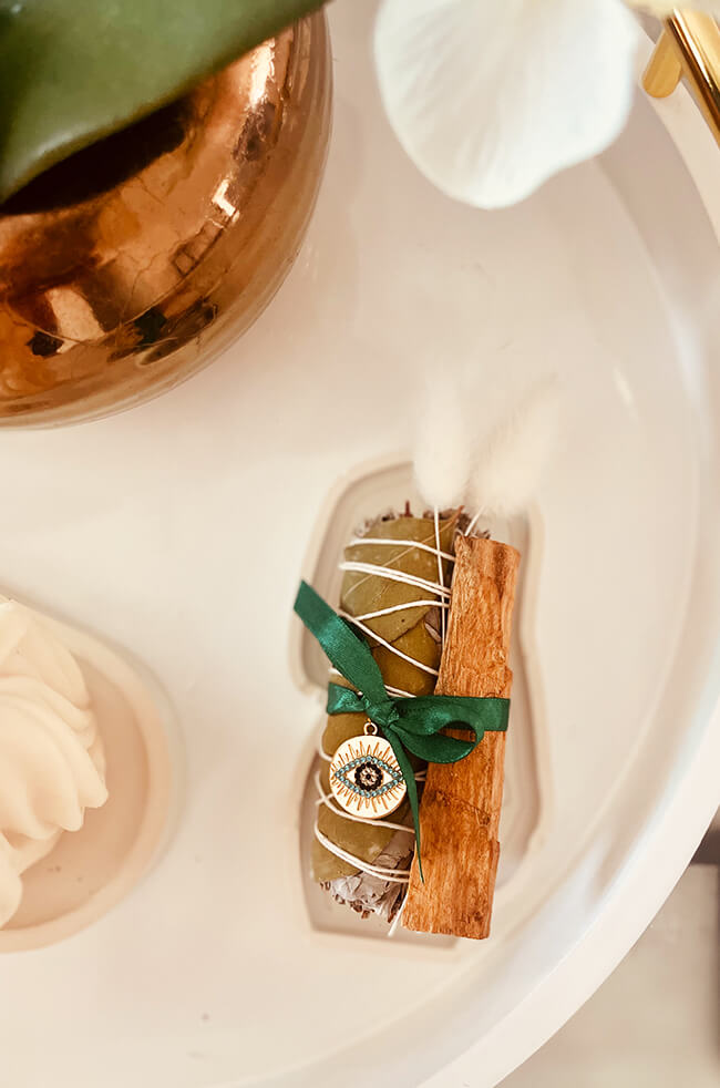 Healing Energy Enhancer Eucalyptus Circle Evil Eye Charm Kit: Eucalyptus, sage, and Palo Santo bundle tied with a green ribbon, decorated with an Evil Eye charm, displayed on a white tray.