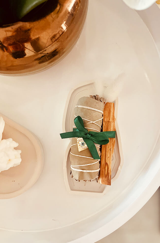 Healing Energy Enhancer Eucalyptus Heart Evil Eye Charm Kit: Eucalyptus, sage, and Palo Santo bundle tied with a green ribbon, decorated with an Evil Eye charm, displayed on a white tray.