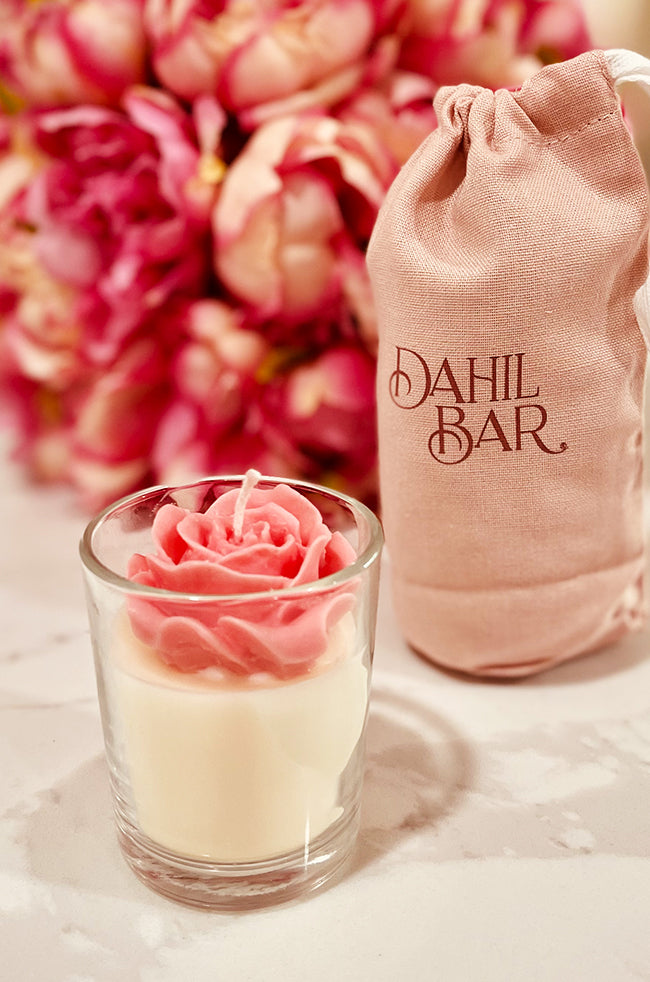 Floating Rose Candle: Pink rose-shaped candle in a glass container, placed beside a pink Dahil Bar cotton bag with blurred pink flowers in the background.
