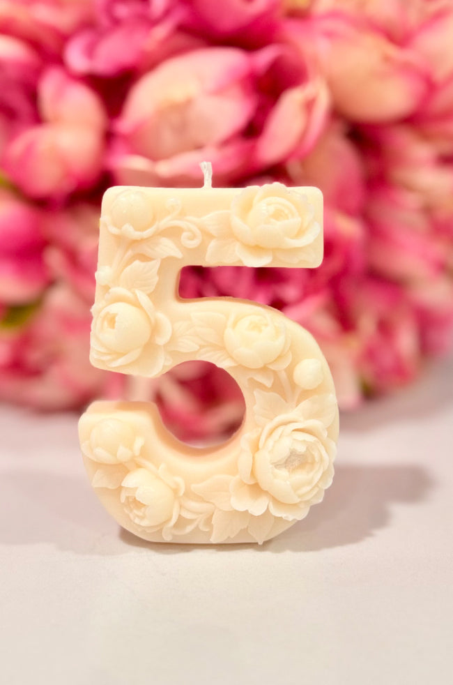 Floral Celebration Number Candle: Ivory floral number 5 celebration candle decorated with roses and delicate botanical details against a pink floral background.