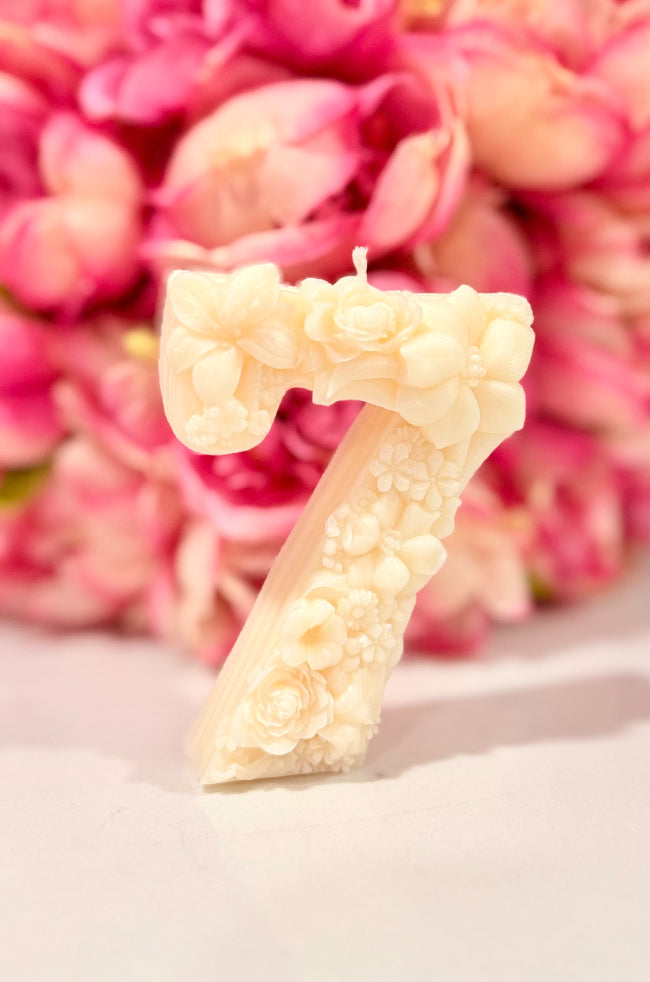 Floral Celebration Number Candle: Ivory floral number 7 celebration candle decorated with roses and delicate botanical details against a pink floral background.