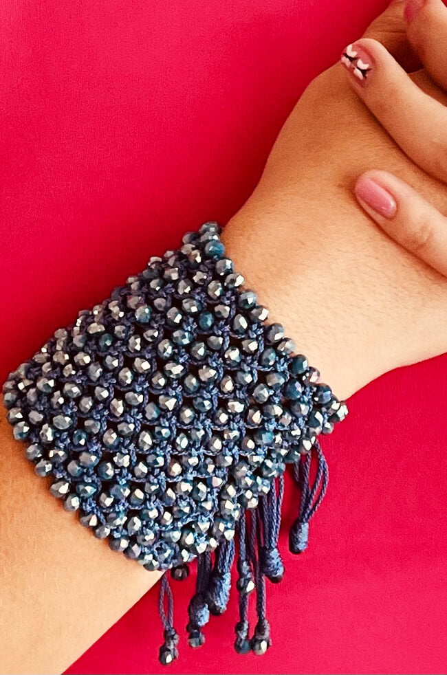 Galaxy Blue: A handmade bracelet featuring dark blue and silver faceted beads intricately woven with navy thread, finished with braided tassels hanging from the edge.