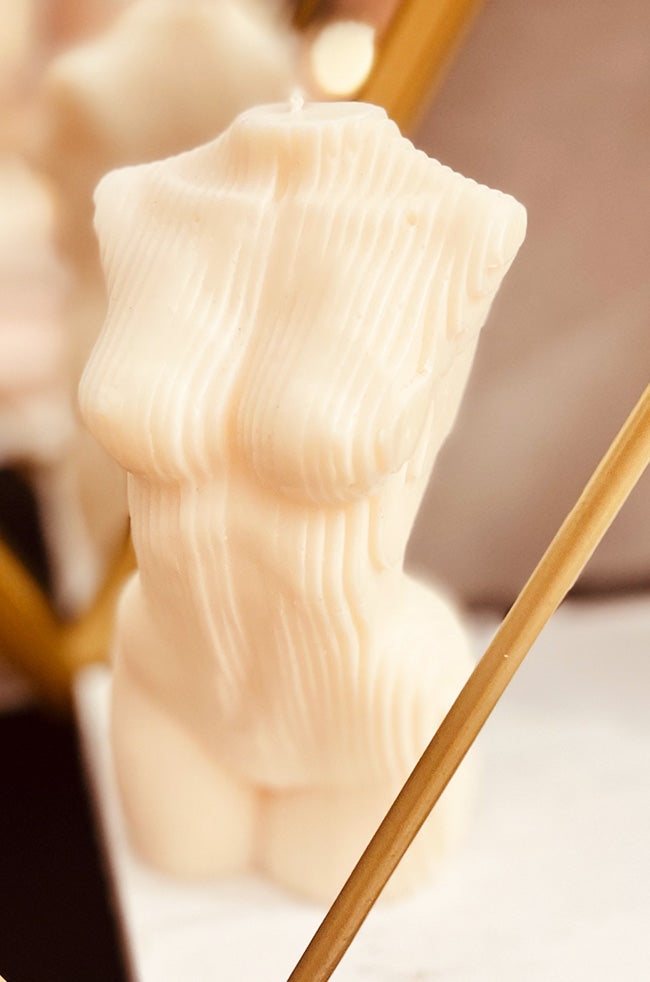 Geometric Venus Candle: Ivory sculptural candle shaped as a stylized female torso with vertical textured lines, displayed in front of a mirror.