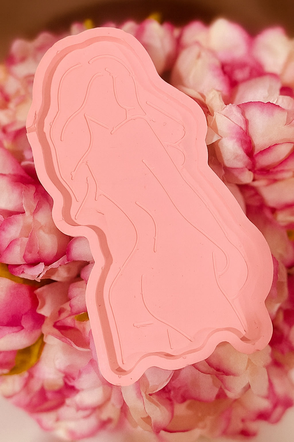Goddess Silhouette Tray Pink: Pink tray with an embossed feminine silhouette design, displayed on a bed of pink flowers.