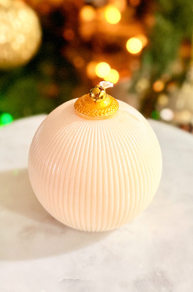 Golden Celestial Ornament Candle: A gold ornament candle with a ribbed texture and gold bell accent, photographed on a marble surface with warm festive bokeh.