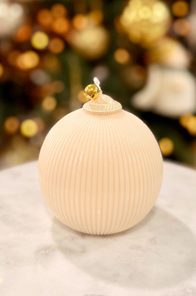 Golden Celestial Ornament Candle: A spherical ribbed pearl candle with a gold bell accent at the wick, photographed against soft holiday bokeh lighting.