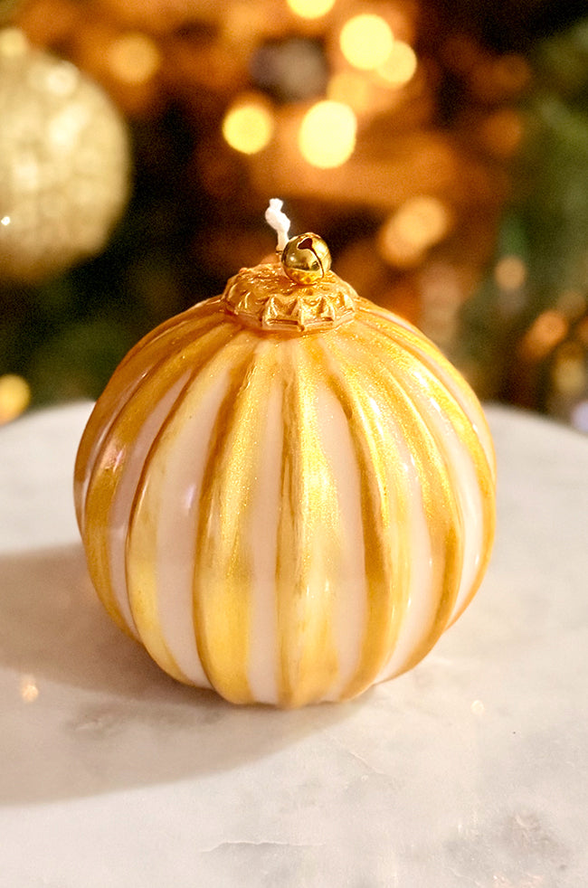 Golden Glow Ornament Candle: Handmade Golden Glow Ornament candle featuring gold-striped detailing, varnished shine, and a gold bell top, styled with warm holiday lights.