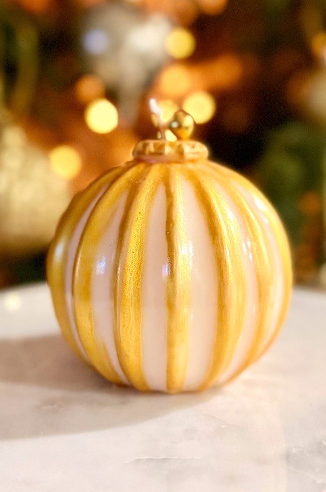 Golden Glow Ornament Candle: Luxury ornament-shaped candle with ivory wax and gold hand-painted stripes, topped with a gold bell, displayed in minimalist holiday décor.
