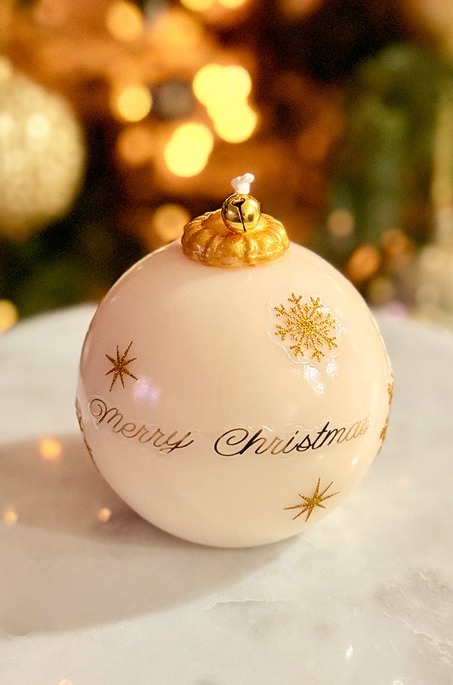 Golden Merry Ornament Candle: Golden Merry Ornament candle showing gold snowflake and star designs on an ivory surface, finished with a shiny varnish and a gold bell topper, styled on marble.