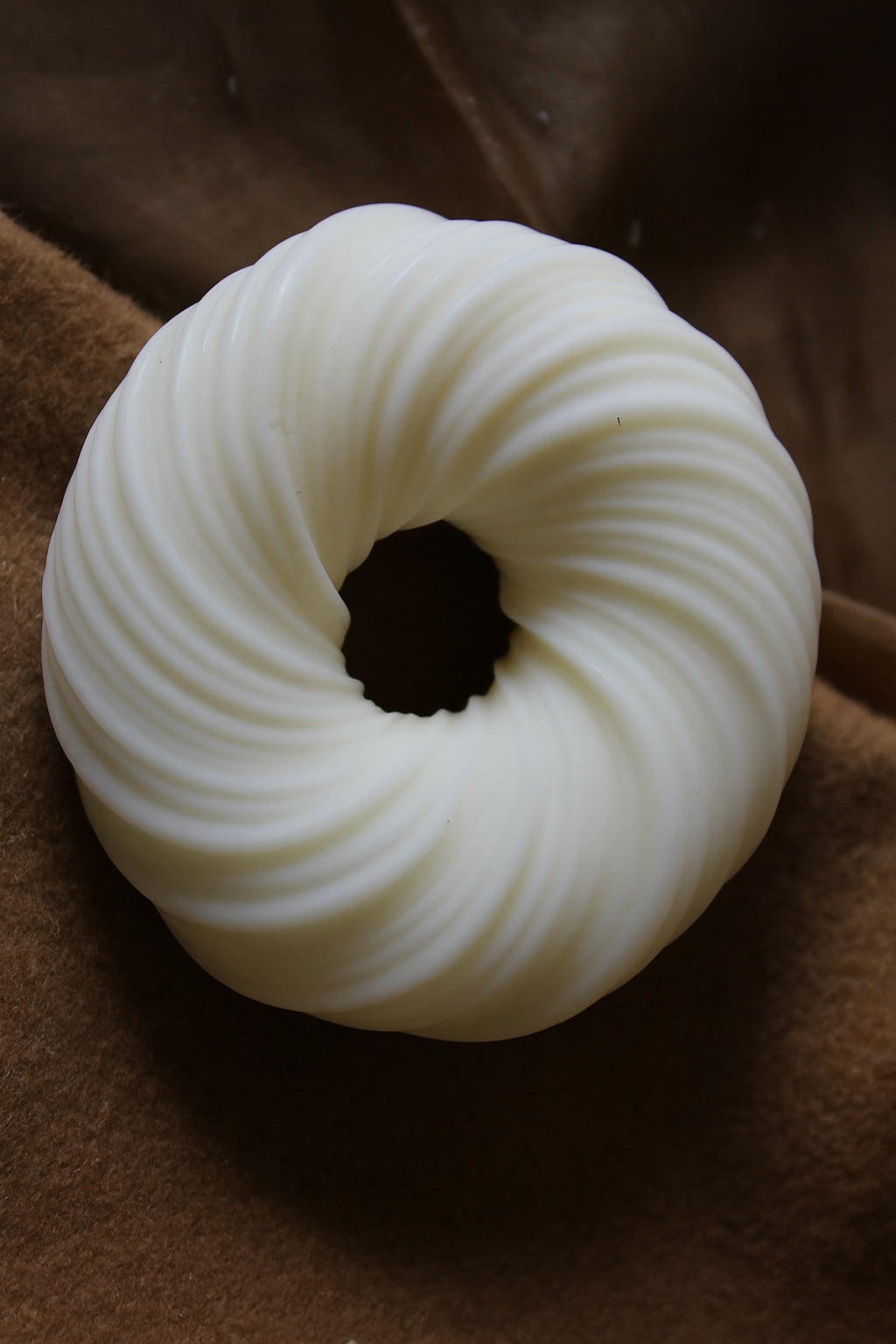 Gyrate Girdle Candle: Ivory round sculptural candle with grooved texture, displayed on a brown fabric background.