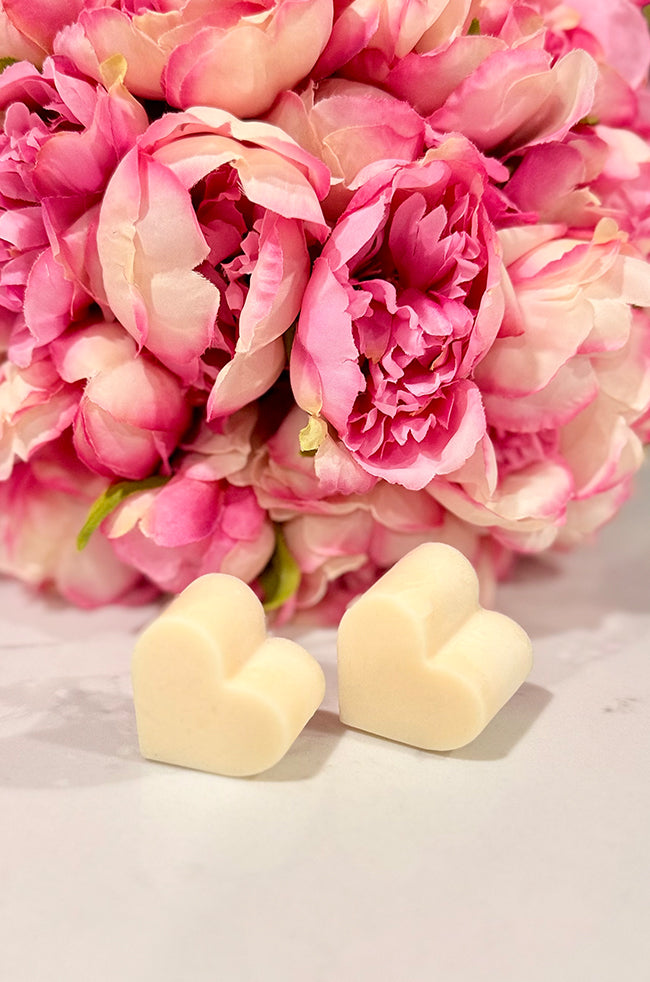 Heart Wax Melts: Two ivory heart-shaped wax melts styled beside a lush pink flower arrangement.