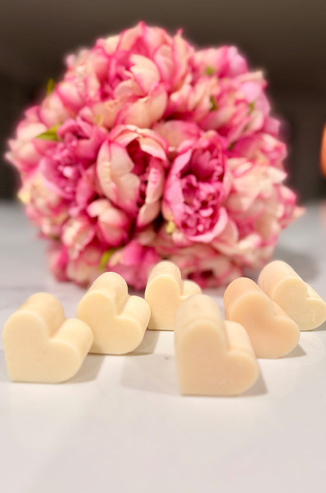 Heart Wax Melts: Ivory heart-shaped wax melts arranged in front of a vibrant pink floral bouquet.