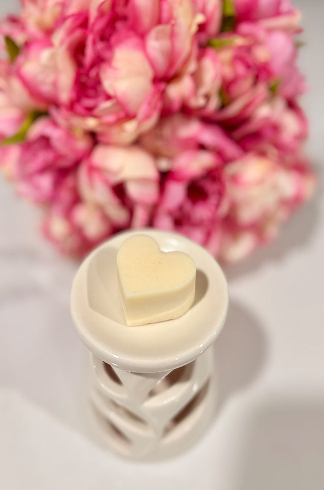 Heart Wax Melts: Ivory Heart Wax Melt displayed on top of a white ceramic wax warmer with pink flowers in the background.