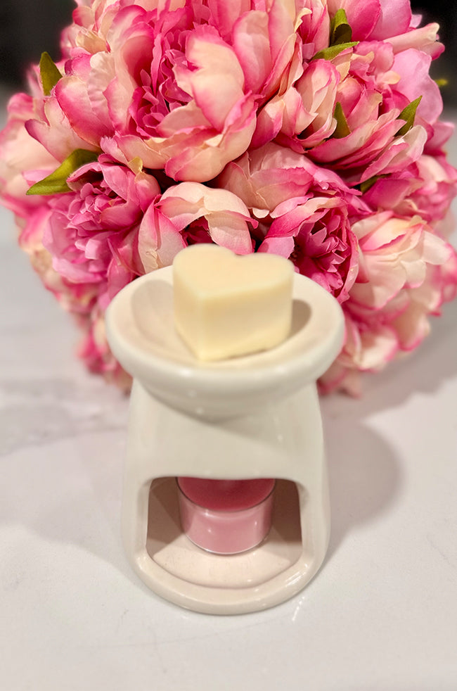 Heart Wax Melts: Heart-shaped wax melt placed on a white ceramic wax warmer with a pink tea light below.