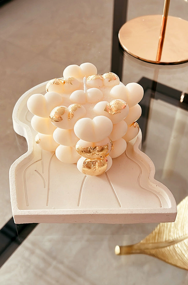 Hearty Bubble Candle: White bubble candle with heart-shaped details and gold accents, displayed on a sculptural white tray.

