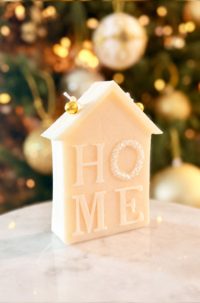 Home for Christmas Candle: Angled view of the Home for Christmas sculptural candle featuring HOME lettering, with a pearl wreath detail and two golden bells against festive holiday décor.