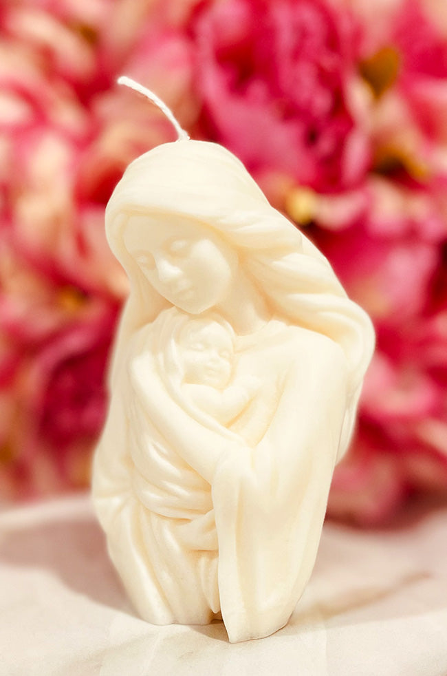 Hugging Oliver Candle: White sculpted candle of a mother tenderly holding a baby, set against a backdrop of pink flowers.