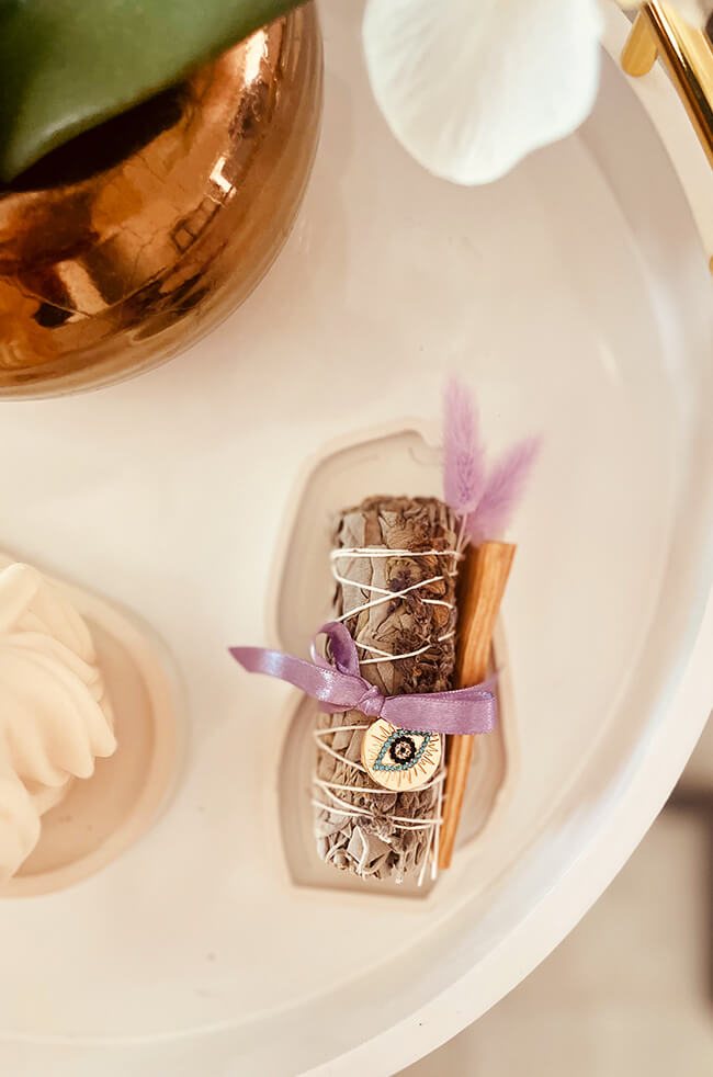 Healing Energy Enhancer Lavender Circle Evil Eye Charm Kit: Lavender, sage, and Palo Santo bundle tied with a purple ribbon and adorned with an Evil Eye charm, displayed on a white tray.
