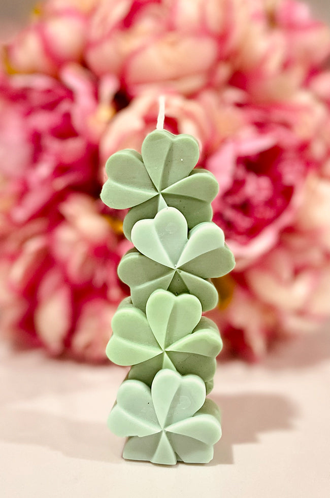 Lucky Clover Candle: Handcrafted green Lucky Clover sculpted candle made of eco-friendly wax, featuring a modern four-leaf clover design, perfect for minimalist and luxury home décor in a floral background.