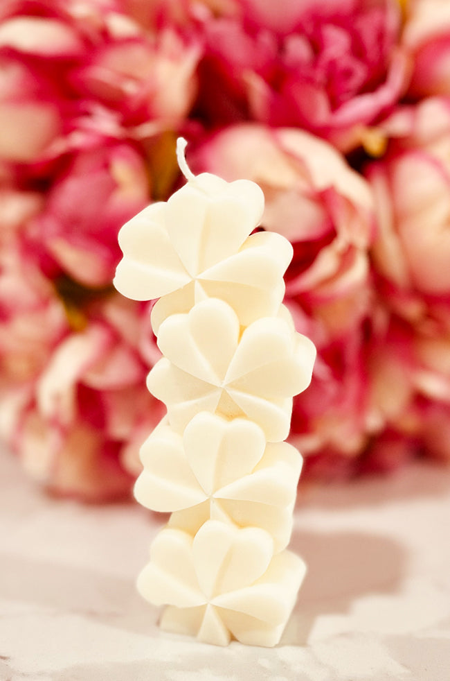 Lucky Clover Candle: Handcrafted Lucky Clover sculpted candle made of eco-friendly wax, featuring a modern four-leaf clover design, perfect for minimalist and luxury home décor in a floral background.