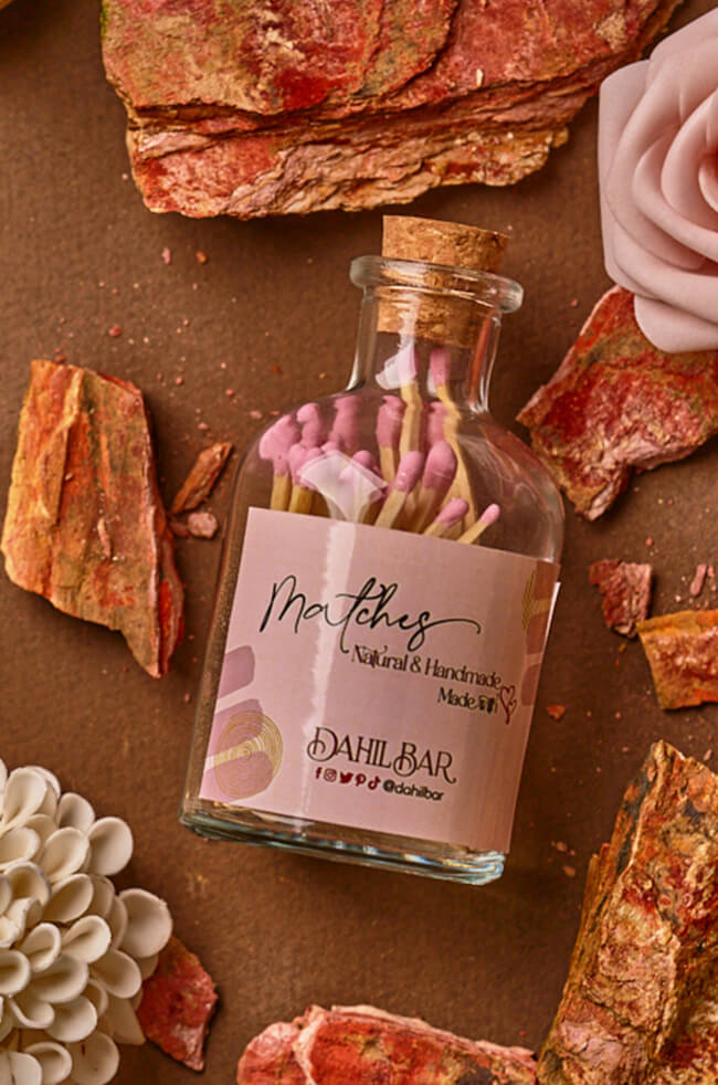 Glass Bottle Matches: Glass bottle filled with pink matches and sealed with a cork, labeled “Dahil Bar,” styled with decorative stones and flowers.