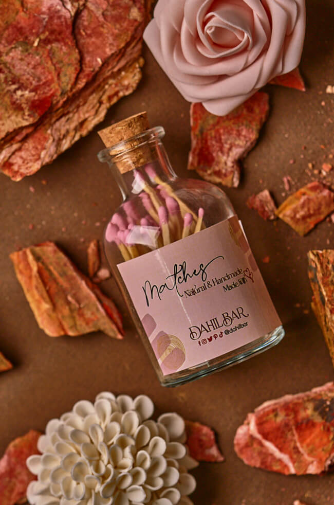 Glass Bottle Matches: Glass bottle of pink matches with a cork lid, labeled “Dahil Bar,” styled with decorative flowers and natural stone accents.