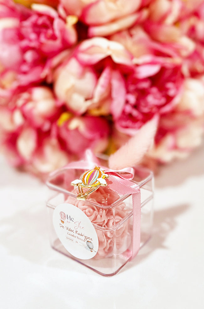 Mini Bloom Gifted Candle: Pink Mini Bloom candle favor in a clear box with ribbon and a hot-air-balloon charm for a gender-reveal celebration.