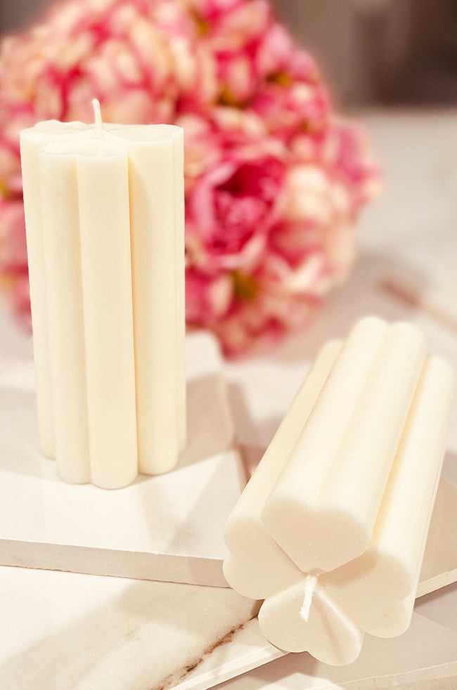 Overlapping Columns Candle: Hand-poured ivory sculptural candle featuring four overlapping columns, resembling a modern trefoil shape, styled on marble with pink florals in the background.