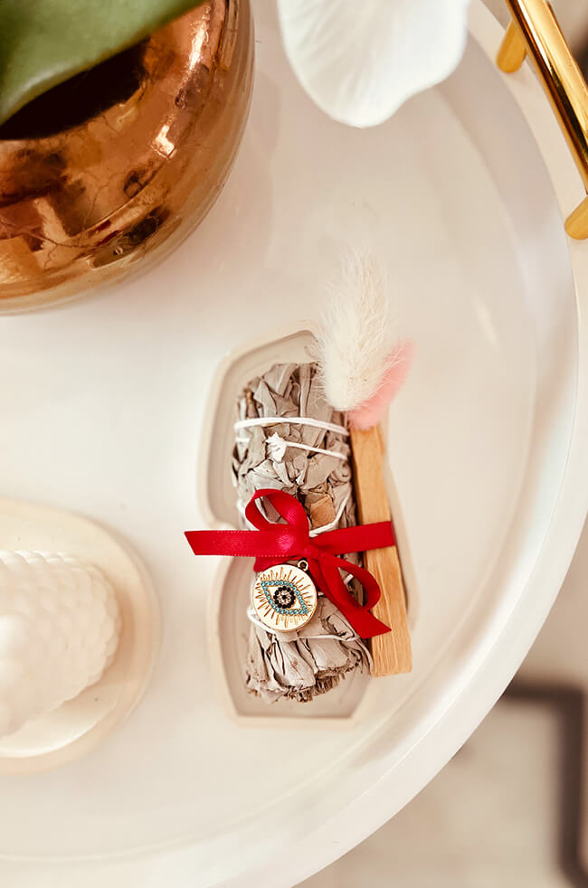 Healing Energy Enhancer White Sage Circle Evil Eye Charm Kit: White sage and Palo Santo bundle tied with a red ribbon and adorned with an Evil Eye charm, displayed on a white tray.