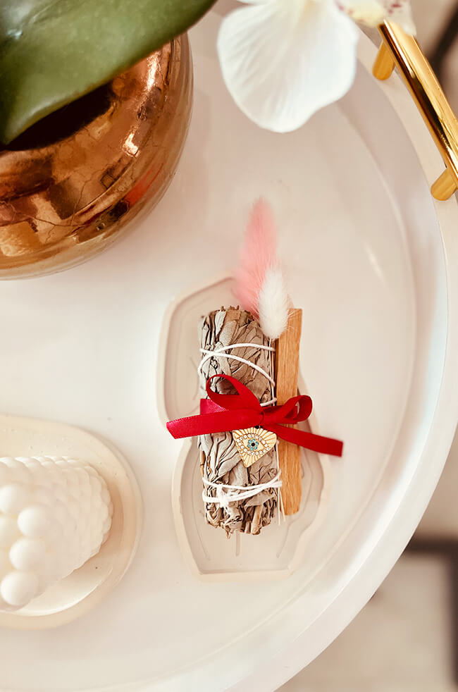 Healing Energy Enhancer White Sage Heart Evil Eye Charm Kit: White sage and Palo Santo bundle tied with a red ribbon and adorned with an Evil Eye charm, displayed on a white tray.