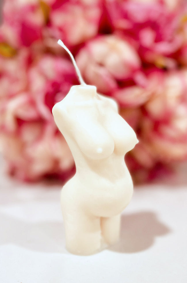 Pregnant Venus Candle: Angled view of the ivory Pregnant Venus pregnancy body candle with pink floral background.