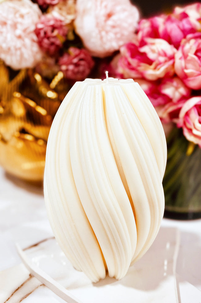 Rising Column Large Candle: featuring a modern twisted column shape with soft pink flowers behind it.