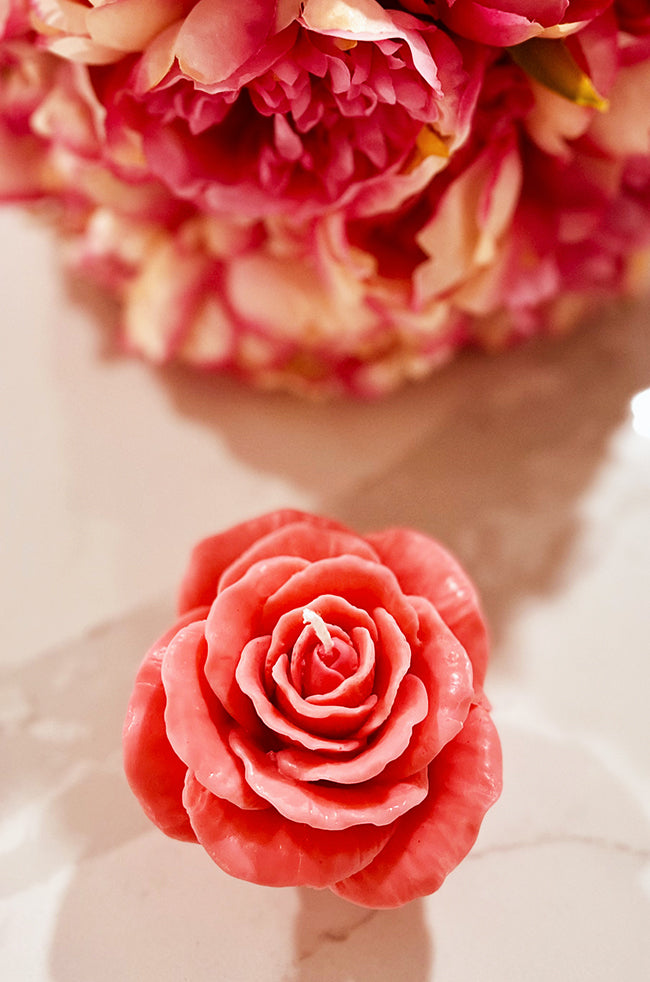 Rose Au Lit Candle: Coral pink Rose Au Lit sculptural rose candle with detailed petals and a soft floral background.