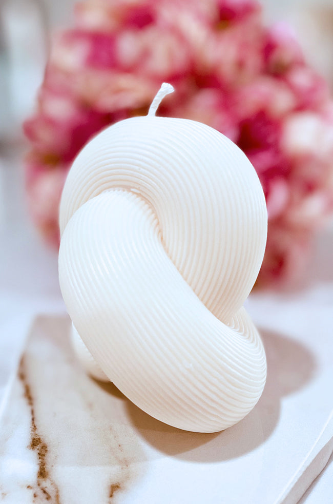 Serenity Knot Candle: Ivory Knot sculptural candle with ribbed texture and intertwined loop design on a marble surface.