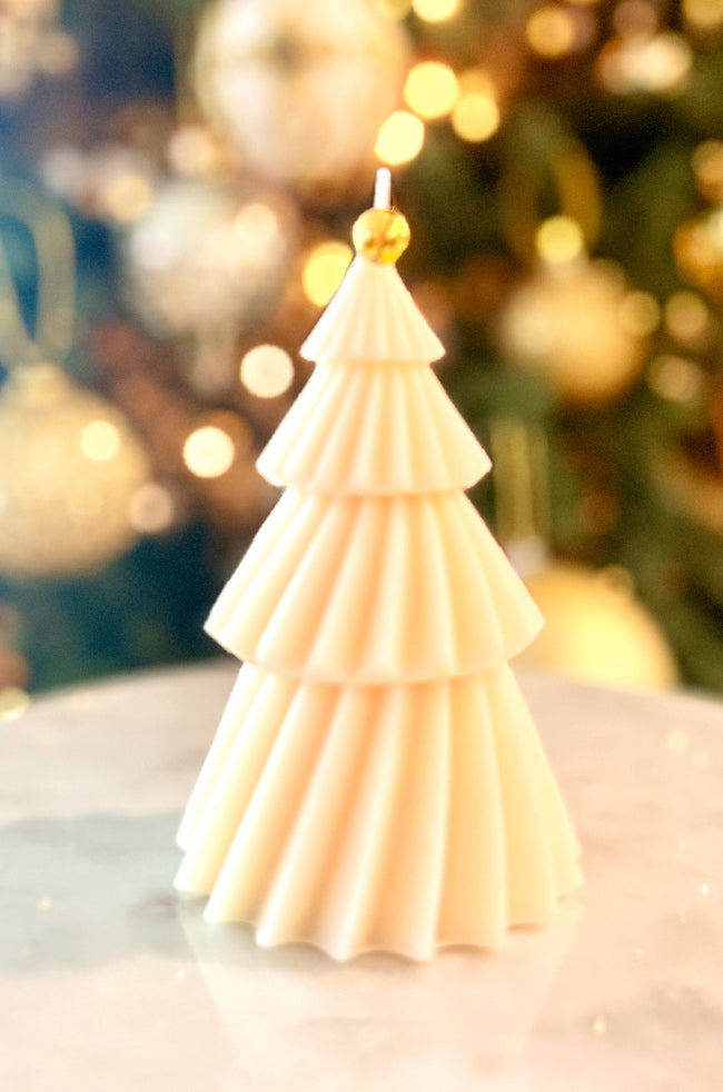 Solstice Tree Large Candle: Elegant sculpted Christmas tree candle with gold foil accents and a gold bell topper, styled against warm golden holiday lights.