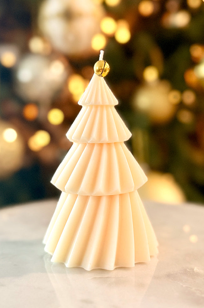 Solstice Tree Large Candle: Handmade Solstice Tree candle featuring gold foil details and a gold bell on top, photographed with a festive, softly blurred background.