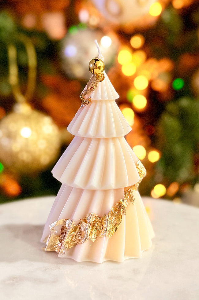 Solstice Tree Large Candle: Cream sculpted tree candle with elegant ridged layers and gold foil accents, placed on marble with blurred golden lights.