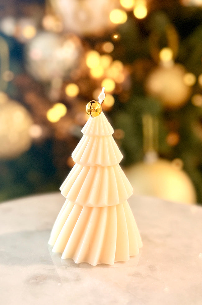 Solstice Tree Small: Elegant tiered candle shaped like a Christmas tree, embellished with vertical gold leaf from top to base, radiating holiday charm against a bokeh-lit Christmas scene.