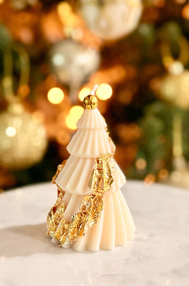 Solstice Tree Small: Holiday tree candle decorated with striking gold leaf wrapping around its layered folds, designed to catch the warm ambient light from the background Christmas décor.