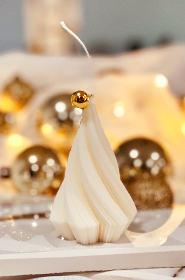 Swirling Fire Tree Small Candle: Minimalist Christmas tree-shaped candle with spiral grooves and gold accent, displayed on a white surface with festive lights.