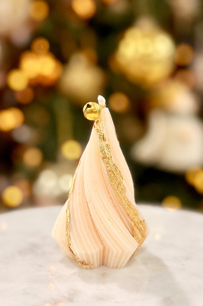 Swirling Fire Tree Small Candle: Hand-poured sculptural candle shaped like a swirling fir tree with gold flakes and a gold bell on top, styled among gold ornaments for the holidays.