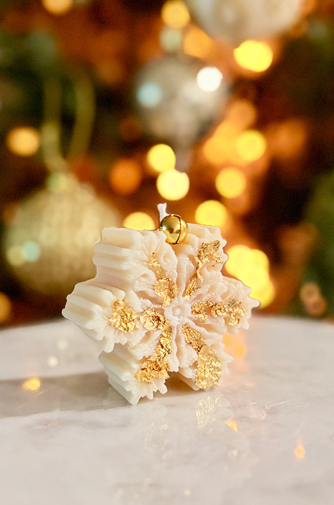 The Christmas Snowflake Candle: Angled view of The Christmas Snowflake candle decorated with gold flakes and topped with a gold bell.
